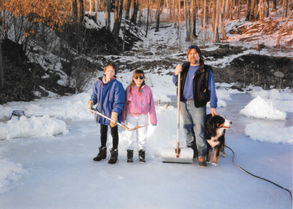 Aly Richards, as a child, and her family are standing on a frozen pond holding shovels. There is a snowy forest in the background.