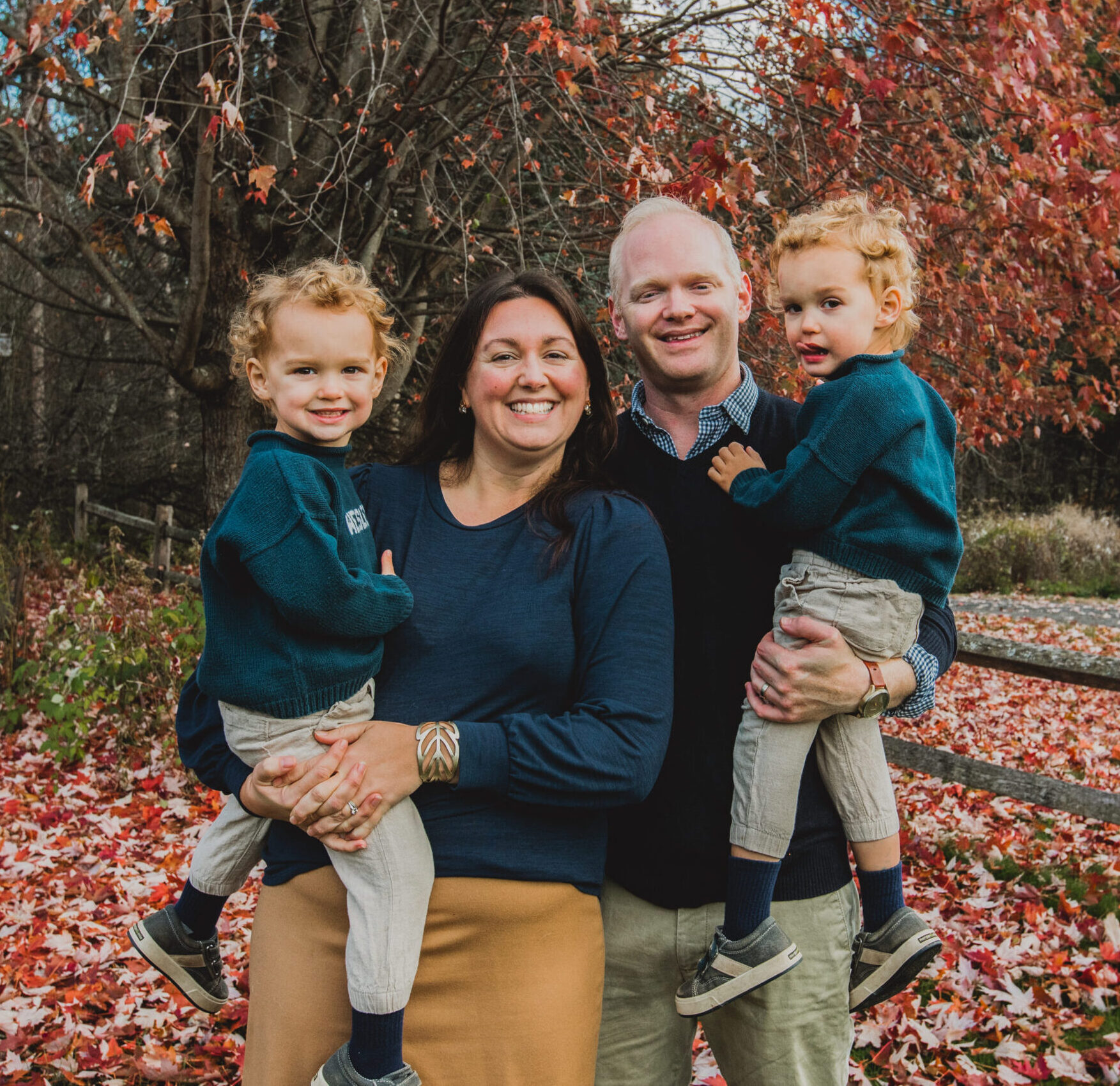 A family portrait of Aly Richards, her husband, and their twin boys. They are standing in front of a tree that has beautiful fall leaves, and are all smiling at the camera.